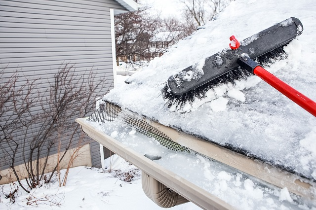 Closeup of a roof snow brush being used to brush snow off of a roof