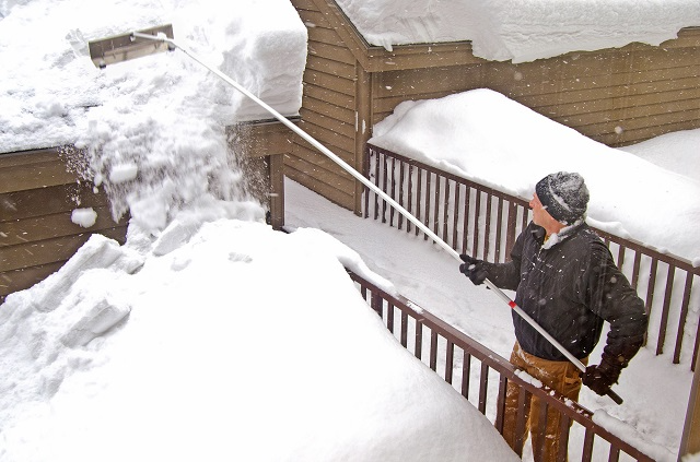 Person using a roof snow shovel to remove snow from a roof while standing on the ground