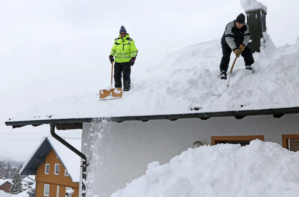 Two people using roof snow shovels to remove snow from a roof