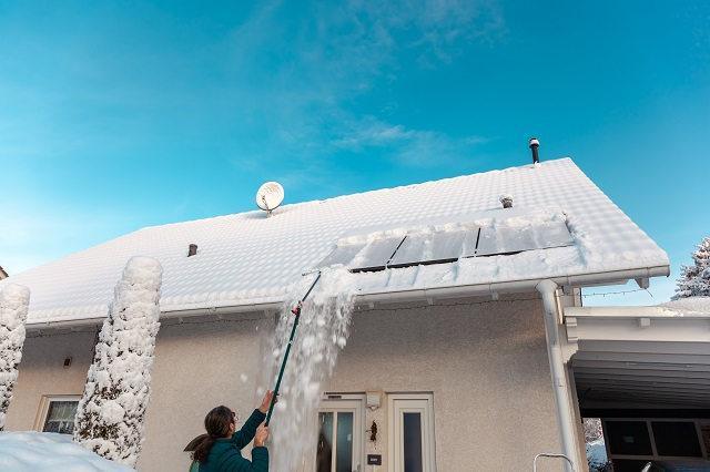 Person using a roof rake to carefully remove snow from a roof with skylights