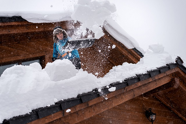 Person shoveling snow off of a roof using a roof snow shovel