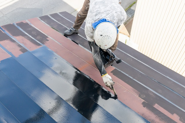 Roofer applying roof sealant or roof coating to a tin roof with a brush