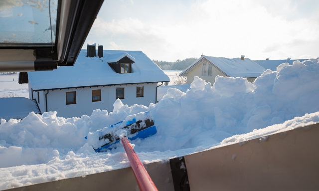 Roof rake for snow, moving snow off the edge of a roof with a house across the street visible over the roof