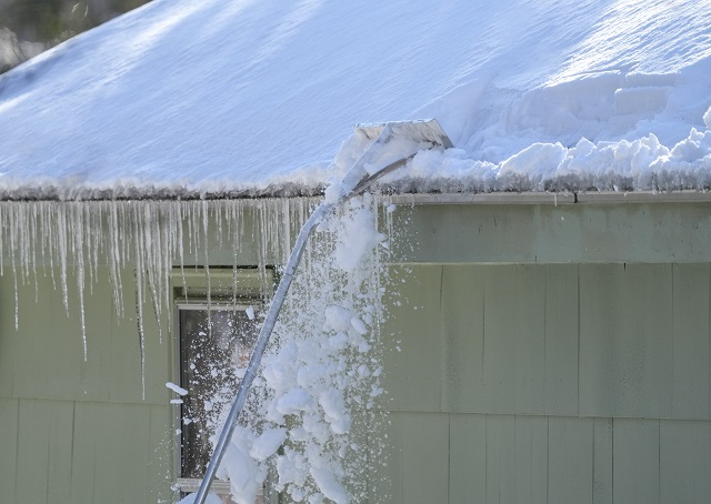 Roof rake with a long handle pulling snow off of the edge of a roof