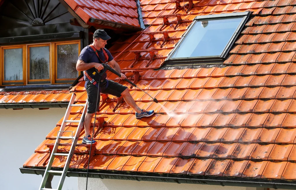 Professional roofer using a pressure washer to clean a tile roof